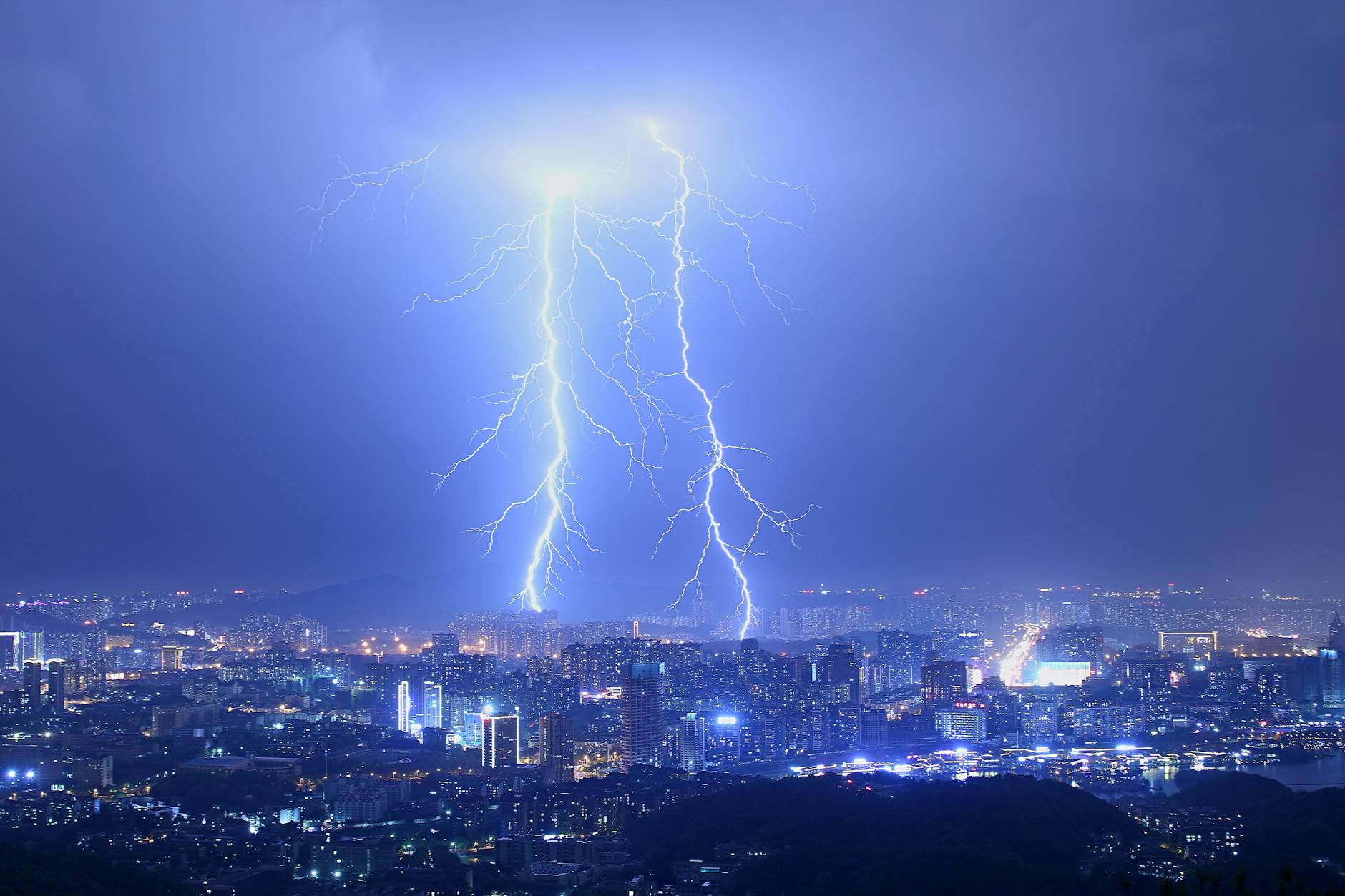 Breathtaking thunderstorm with lightning bolts over modern illuminated city at night with purple sky