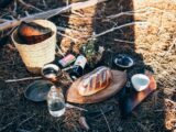 Bread and utensil near bottles and basket on grass