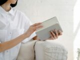 Crop unrecognizable female in white shirt sitting on sofa and opening notepad in light room