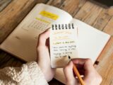 A person holding a pen and writing in a notebook