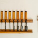 Collection of metal chisels with wooden handles and wood cutters for woodwork arranged on shelf on white wall in workshop