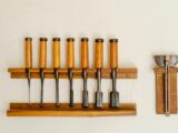 Collection of metal chisels with wooden handles and wood cutters for woodwork arranged on shelf on white wall in workshop