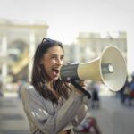 Cheerful young woman screaming into megaphone