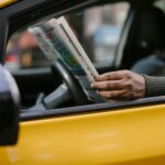 Side view of crop anonymous ethnc male driver reading information in newspaper article while waiting for client