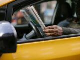 Side view of crop anonymous ethnc male driver reading information in newspaper article while waiting for client