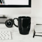 Coffee cup placed on table near computer and notepad with smartphone