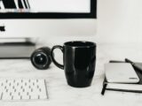 Coffee cup placed on table near computer and notepad with smartphone