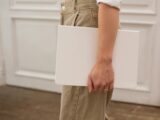 Side view of unrecognizable female in stylish jeans with white blank notebook in hand standing in light room near door