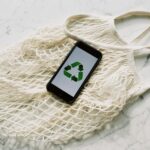 Overhead of smartphone with simple recycling sign on screen placed on white eco friendly mesh bag on marble table in room