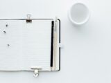 Top view composition of opened diary with blank pages placed on white desk with pencil and paintbrush pins