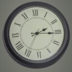 Round black mechanical clock with Roman numerals hanging on gray wall