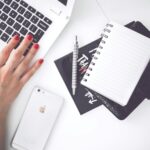 White laptop, female hand, note, pen, phone, desk