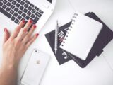 White laptop, female hand, note, pen, phone, desk