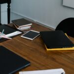 From above of modern laptop and tablet placed on wooden table with various notebooks in workplace