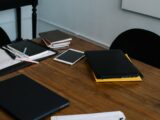 From above of modern laptop and tablet placed on wooden table with various notebooks in workplace