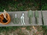 Top view of row of scissors secateurs shovels and tools for loosening soil near pot with instruments on wooden bench in garden