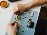 Hands of Person Assembling Transistors with Use of Magnifying Glass