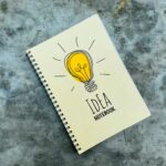 Top view of creative spiral notebook with yellow light bulb illustration on cover placed on gray table