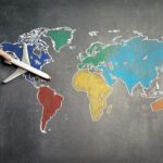 Top view of crop anonymous person holding toy airplane on colorful world map drawn on chalkboard