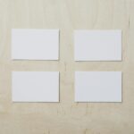 Overhead view of clean white mockup greeting cards placed on light brown wooden desk