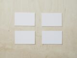 Overhead view of clean white mockup greeting cards placed on light brown wooden desk