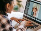 Crop ethnic freelancer retouching photo on laptop at home