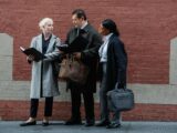 Serious diverse partners examining documents together on city street