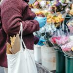 Woman with paper cup of coffee buying flowers on street